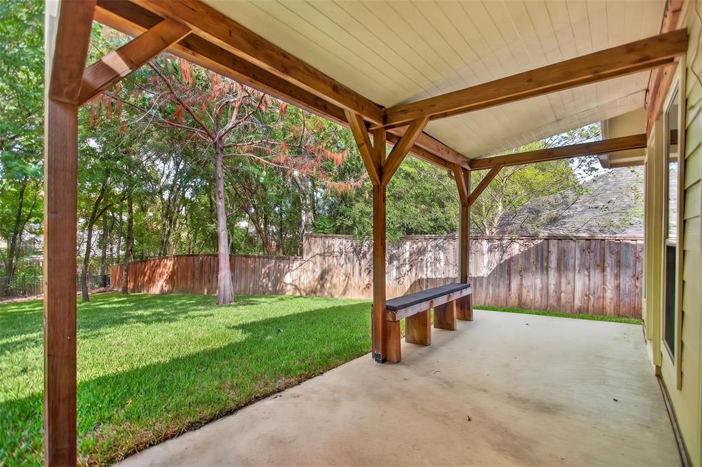 Covered patio featuring a wood-frame structure, built-in timber seating, a concrete floor, and an exterior wood privacy fence enclosing a grass lawn
