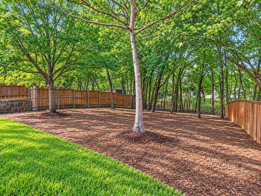 Backyard featuring mature trees, a manicured lawn, wood-panel fencing, and stone retaining wall