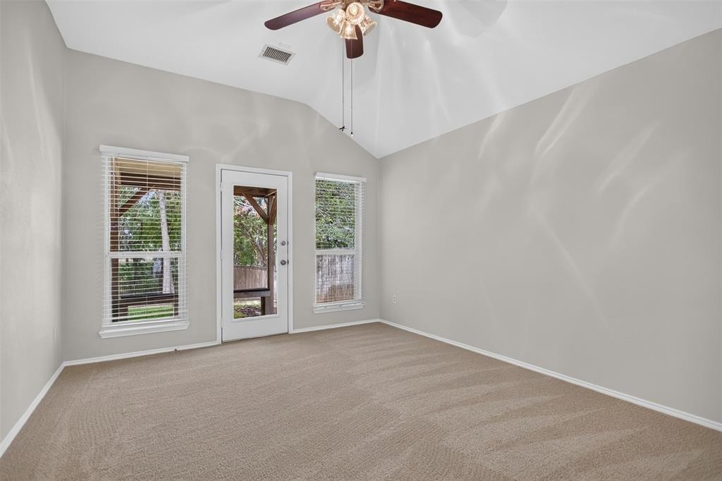 Vaulted ceiling featuring a central lighted ceiling fan, neutral wall tones, wall-to-wall carpeting, and an exterior door flanked by dual windows