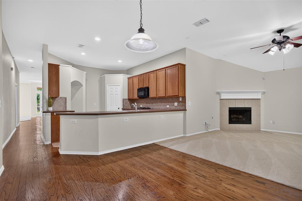 Open-concept area featuring wood-finish flooring, a kitchen with cabinetry and a breakfast bar, vaulted ceilings, and a fireplace with a tile surround