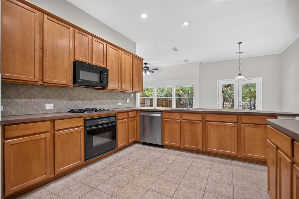 Kitchen featuring medium-toned wood cabinetry, stone-style tile backsplash, stainless steel dishwasher, built-in black gas cooktop and oven, and recessed lighting Kitchen featuring medium-toned wood cabinetry, stone-style tile backsplash, stainless steel dishwasher, built-in black gas cooktop and oven, and recessed lighting
