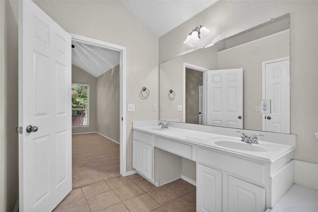 Dual-sink vanity with white cabinetry, solid-surface countertop, full-width wall mirror, and ceramic tile flooring