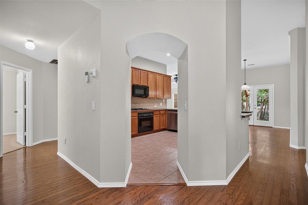 Interior featuring wood-finish flooring, an arched entryway, tile flooring in the kitchen, built-in cabinetry, and a glass-paned exterior door Interior featuring wood-finish flooring, an arched entryway, tile flooring in the kitchen, built-in cabinetry, and a glass-paned exterior door