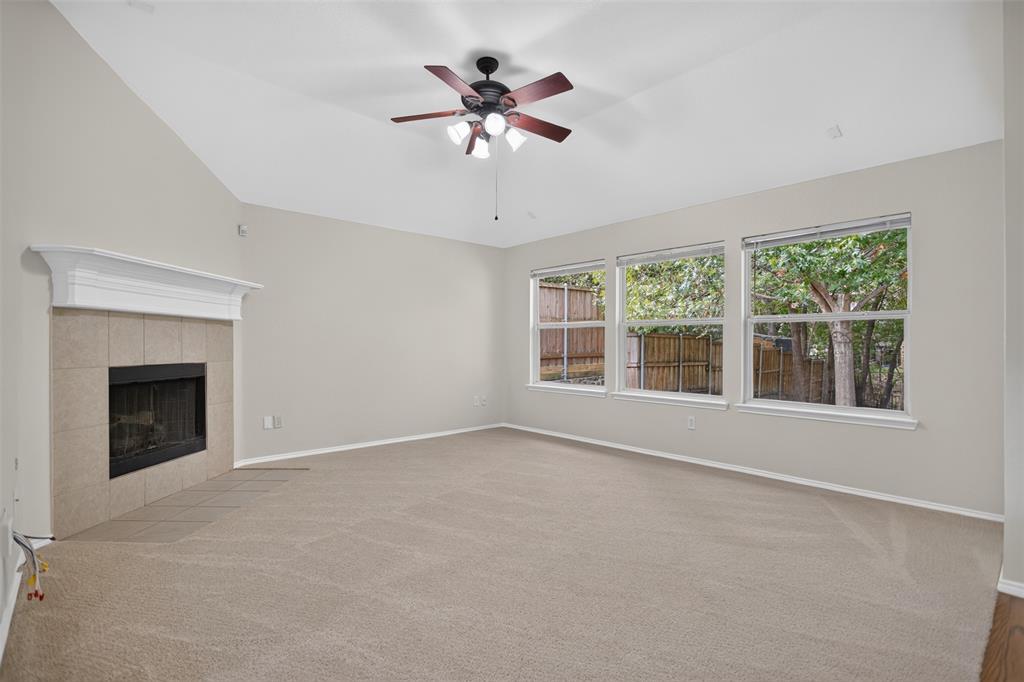 Vaulted ceilings, neutral carpeting, a fireplace with a mantel and tile surround, and a ceiling fan with integrated lighting