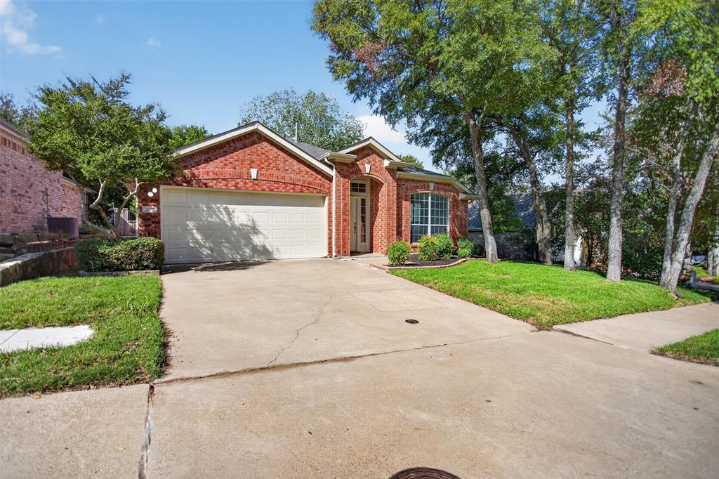 Single-story brick exterior featuring a front-facing attached two-car garage, arched entryway, and mature trees situated on a landscaped lot Single-story brick exterior featuring a front-facing attached two-car garage, arched entryway, and mature trees situated on a landscaped lot