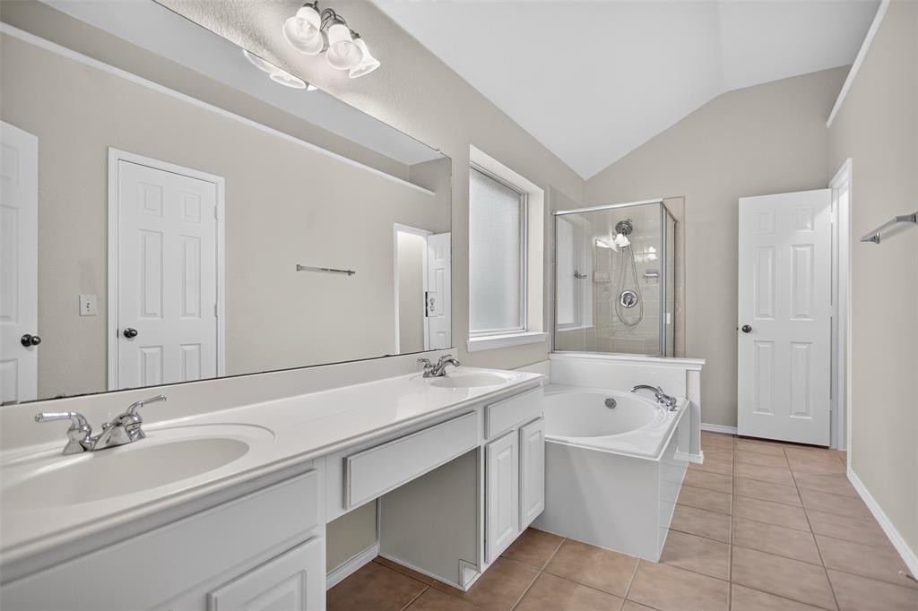 Bathroom featuring a dual-sink vanity with white cabinetry, a large wall-to-wall mirror, an integrated soaking tub, and a glass-enclosed shower