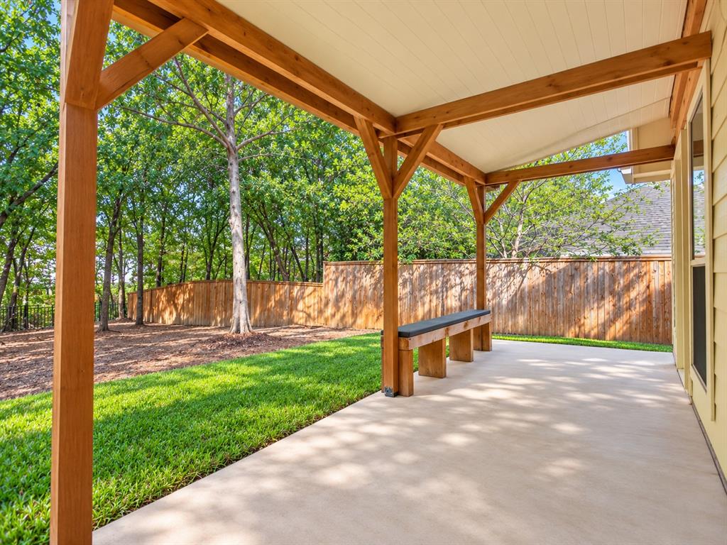 Covered patio featuring a timber-frame pergola, concrete flooring, built-in wooden bench, and backyard with grass lawn and wood fencing