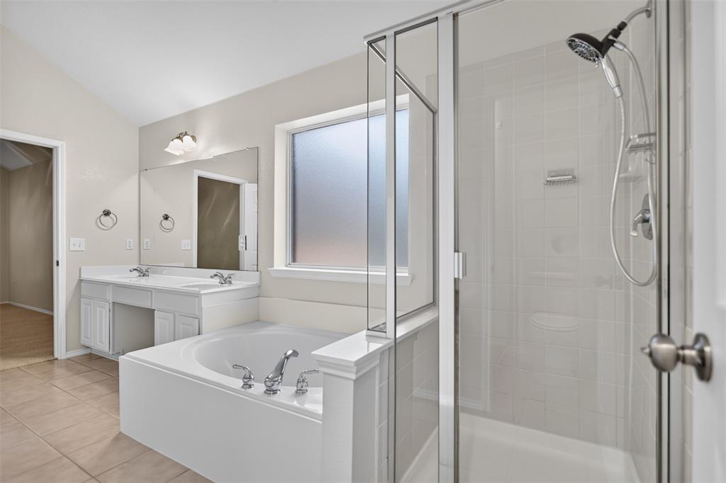 Bathroom featuring a glass-enclosed shower, soaking tub, dual-sink vanity with countertop, and tile flooring