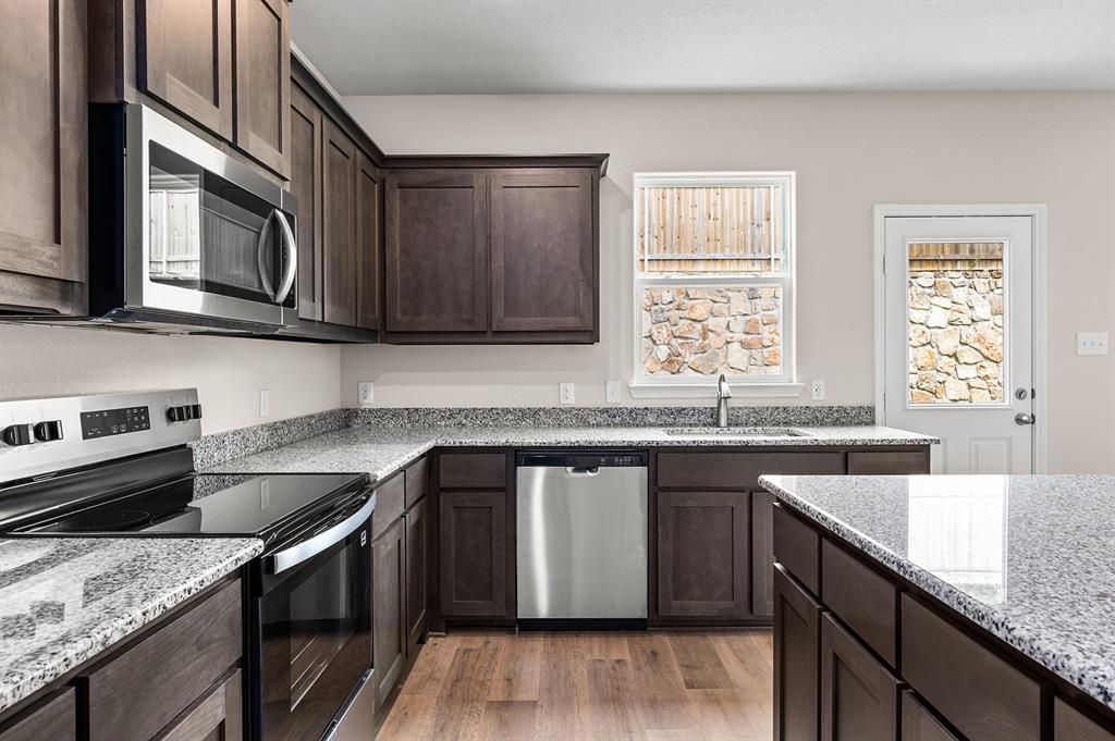 Kitchen with appliances with stainless steel finishes, light wood-style flooring, dark brown cabinetry, and light stone counters