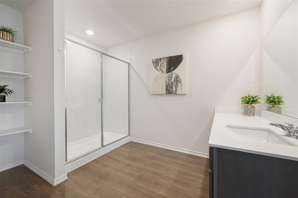 Shower enclosure with metal framing, vanity featuring a solid surface countertop, built-in shelving, full-width vanity mirror, and wood-finish flooring
