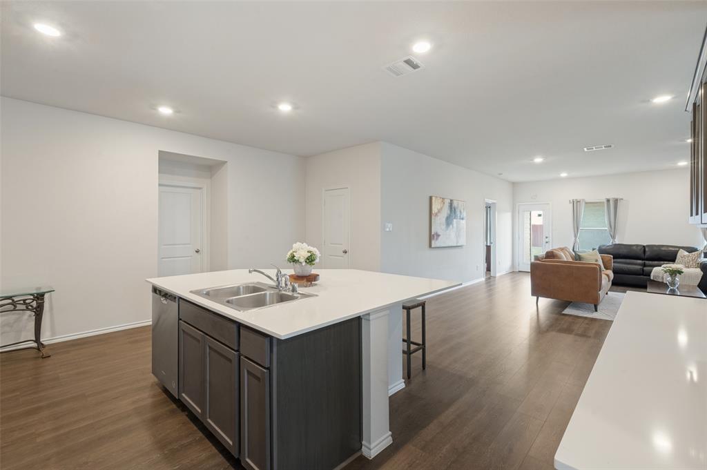 Kitchen featuring a central island with a solid-surface countertop, stainless steel dual-basin sink, recessed lighting, and wood-finish flooring