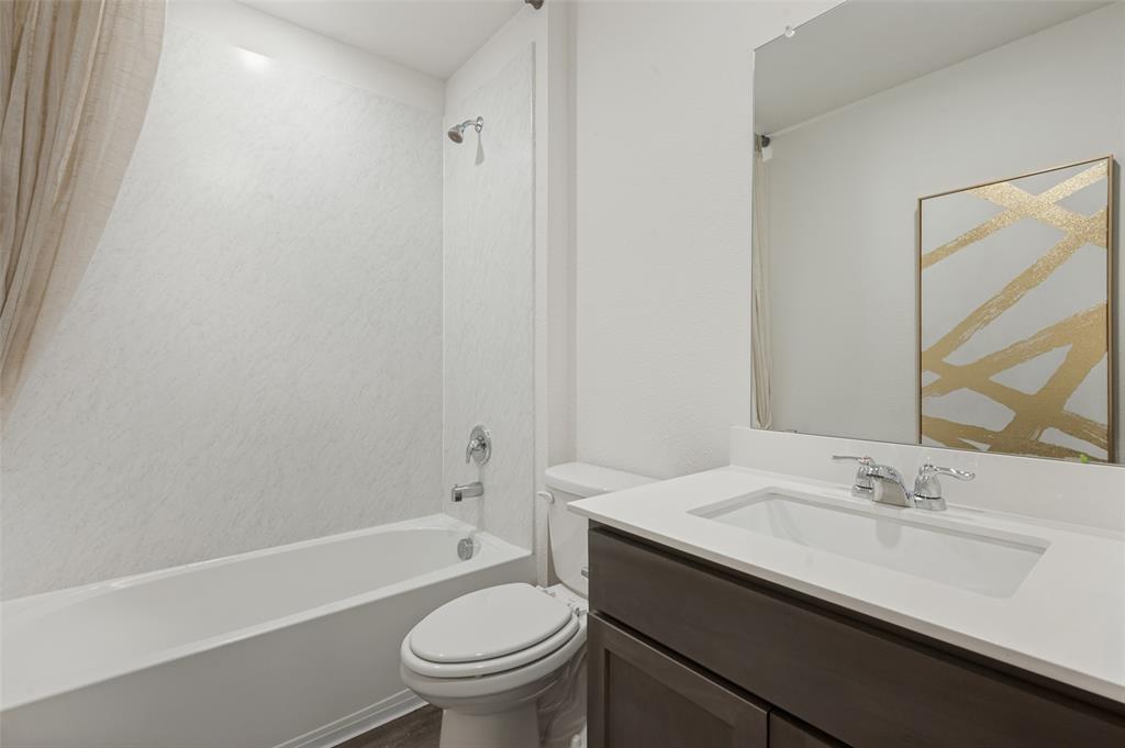 Bathroom featuring a vanity with a white countertop and rectangular undermount sink, a large wall-mounted mirror, and a tub-shower combination with surround wall paneling