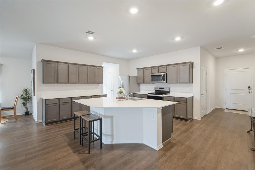 Kitchen featuring grey cabinetry, white countertops, an oversized central island, stainless steel appliances, and wood-finish flooring