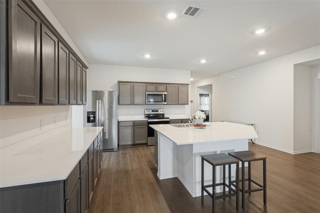 Kitchen featuring dark-toned cabinetry, solid-surface countertops, a center island, stainless steel appliances, and wood-finish flooring