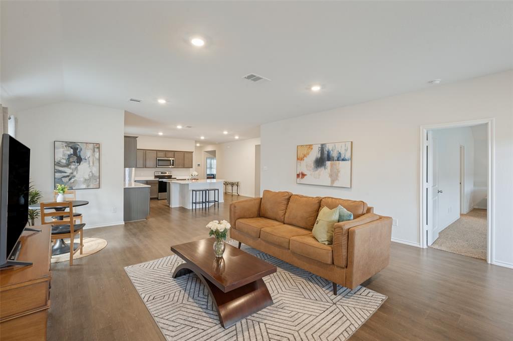 Open-concept main living area featuring recessed lighting, vaulted ceilings, wood-finish flooring, and a kitchen equipped with a central island and shaker-style cabinetry