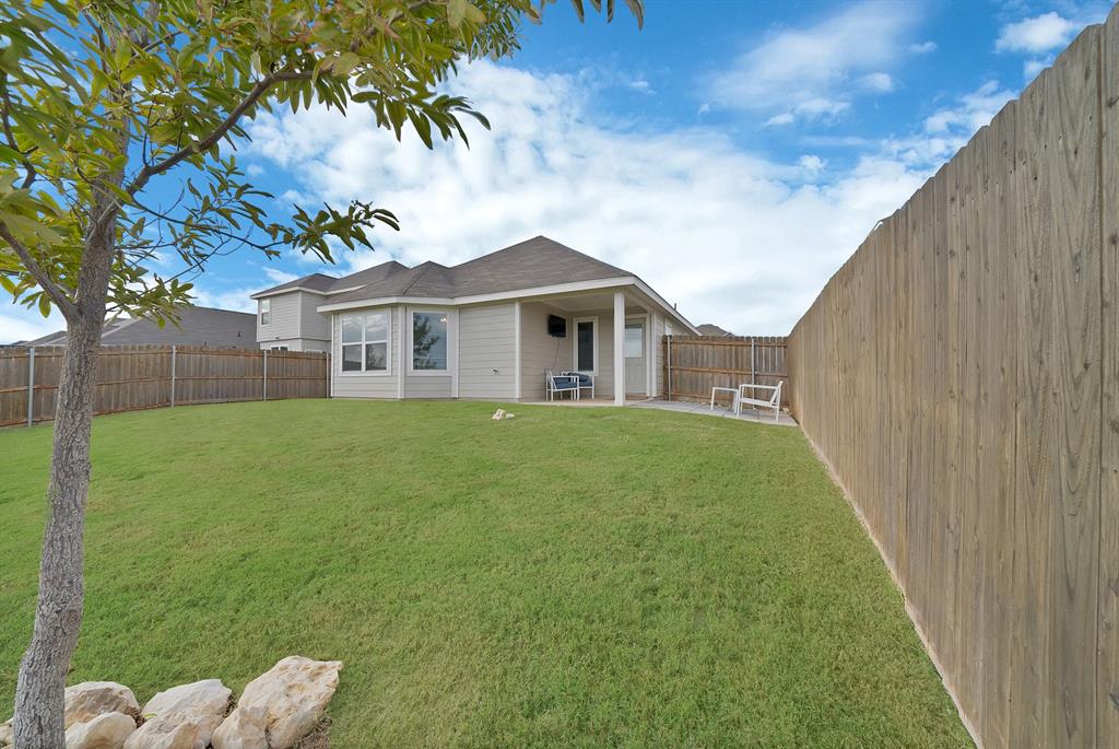 Fenced backyard featuring a manicured lawn, covered concrete patio, and decorative stone landscaping elements