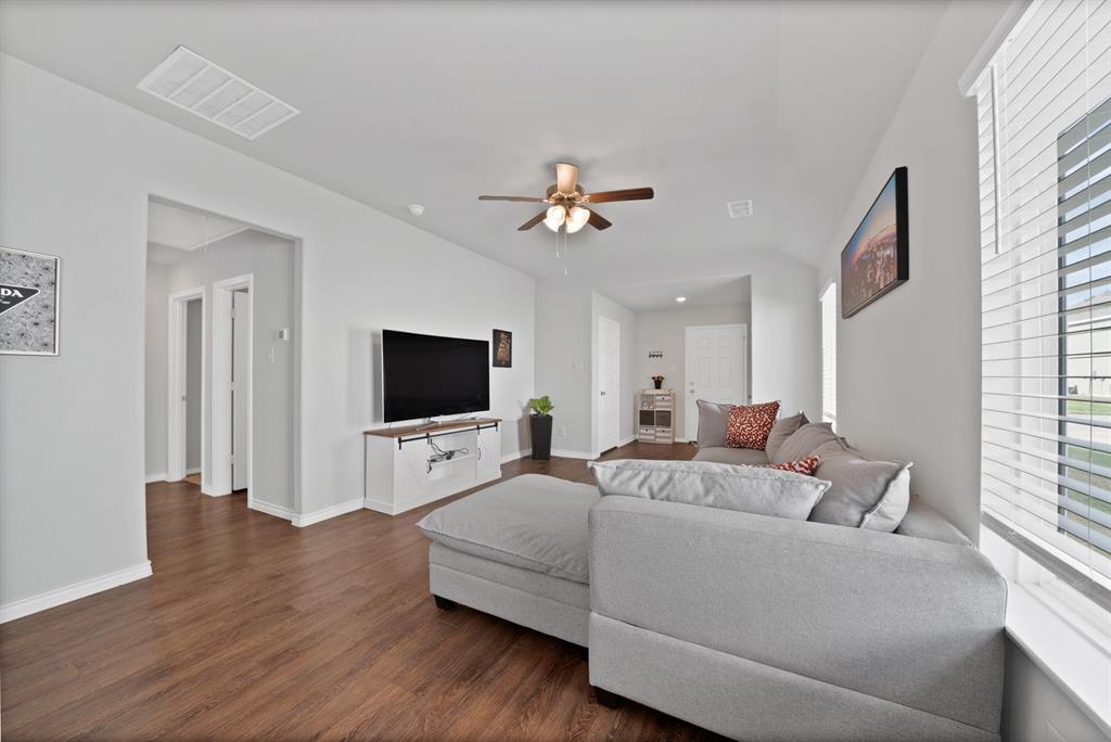 Living area featuring wood-finish flooring, high ceilings, a central ceiling fan with integrated lighting, and horizontal window blinds