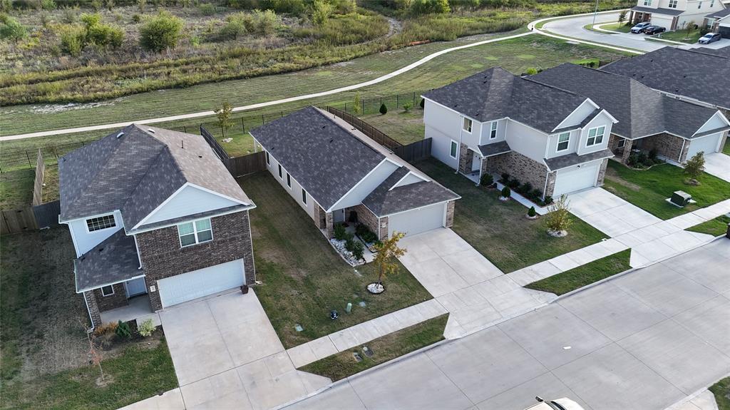 Aerial perspective of residential exteriors featuring mixed brick and siding facades, shingled roofing, concrete driveways, and backyards bordered by a winding trail