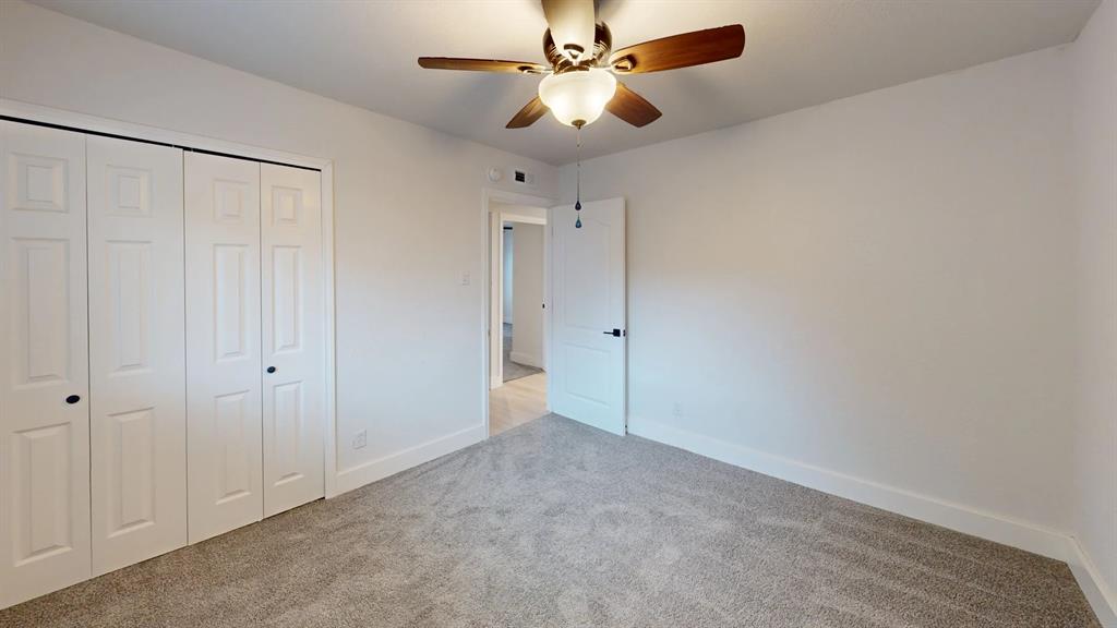 Neutral interior room featuring neutral carpeting, a ceiling fan with integrated lighting, and white bi-fold closet doors