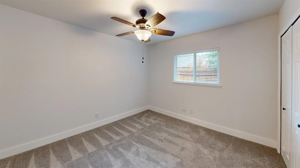 Neutral-toned wall-to-wall carpeting, ceiling fan with integrated light fixture, dual-panel closet doors, and sliding window
