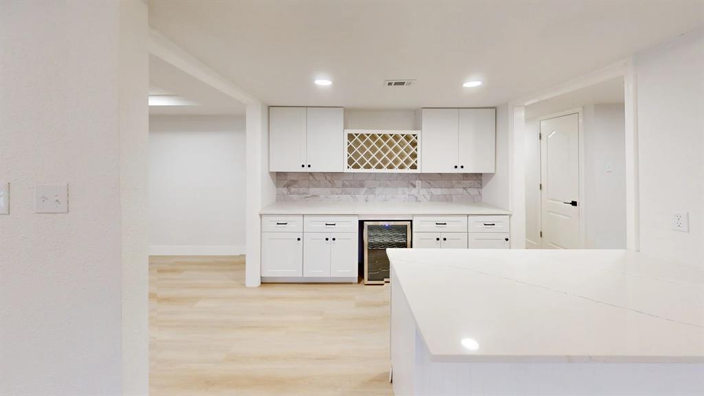 White shaker-style cabinetry, integrated wine refrigerator, built-in wine rack, quartz countertop, and patterned stone-finish backsplash
