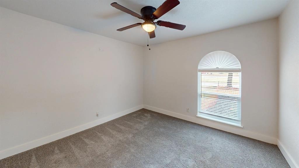 Neutral-toned carpeted flooring, vaulted arched window, and overhead ceiling fan with light fixture