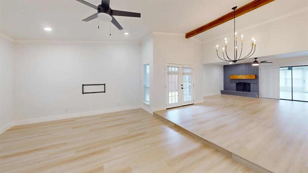 Vaulted ceiling with exposed decorative wood beam, wood-finish flooring, metal multi-arm chandelier, and floor-to-ceiling brick fireplace with a wood mantel