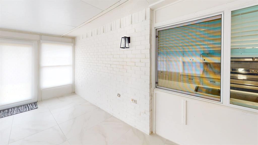 Enclosed sunroom featuring white painted brick walls, large format tile flooring, and wall-mounted exterior-style lantern lighting