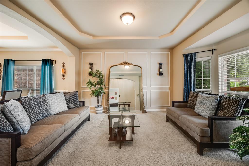 Living room with a raised ceiling, arched walkways, carpet flooring, and a decorative wall