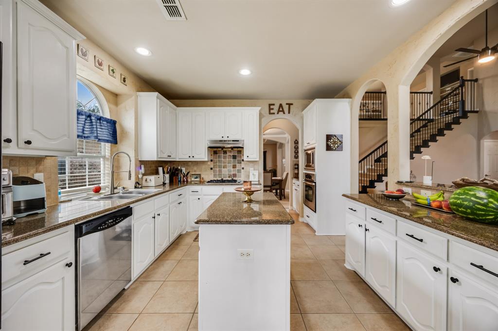 Kitchen featuring arched walkways, dark stone counters, white cabinets, light tile patterned floors, and backsplash