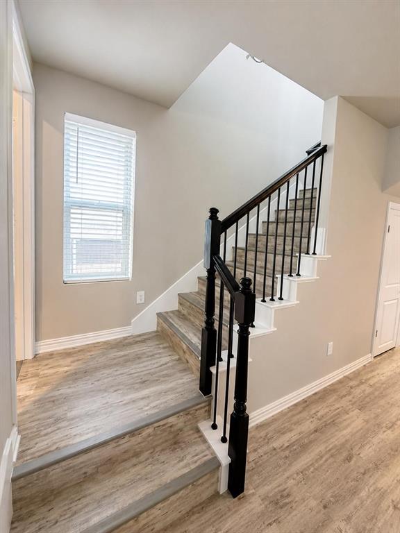 Staircase featuring wood-finish flooring, white risers, black metal balusters, and a dark stained wood handrail