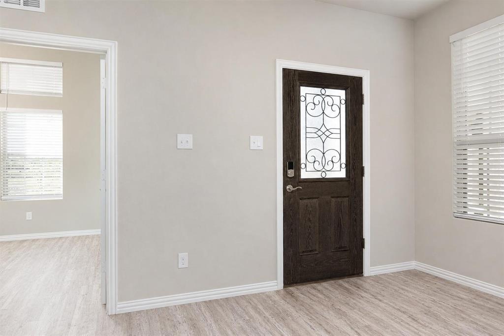 Dark-finished wood entry door featuring decorative iron grillwork, horizontal wood-finish flooring, and window blinds