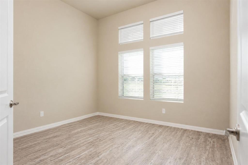 Room featuring high ceilings, wood-finish flooring, and four stacked windows with horizontal blinds