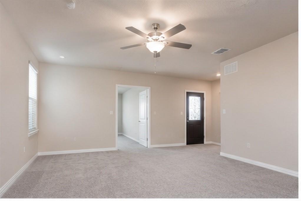 Neutral-toned interior space featuring neutral wall paint, wall-to-wall carpeting, a ceiling fan with integrated lighting, and a dark-finished exterior door with a glass insert