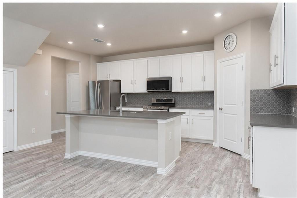 Kitchen featuring white cabinetry, solid-surface countertops, a center island with a stainless steel sink, hexagonal tile backsplash, and wood-finish flooring