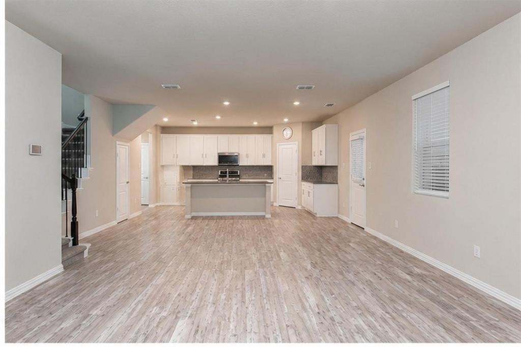 Open-concept interior featuring wood-finish flooring, recessed lighting, white cabinetry, a center island, and a staircase with a dark-finished handrail