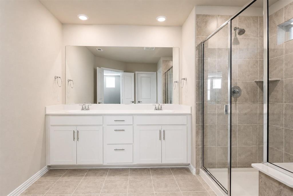Double vanity with white cabinetry, solid surface countertop, expansive wall mirror, and walk-in shower featuring tiled walls and a glass enclosure