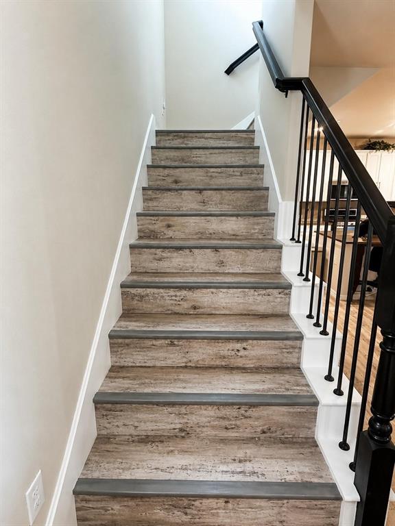 Staircase featuring wood-finish treads, painted risers, and a matte black metal railing with a matching handrail