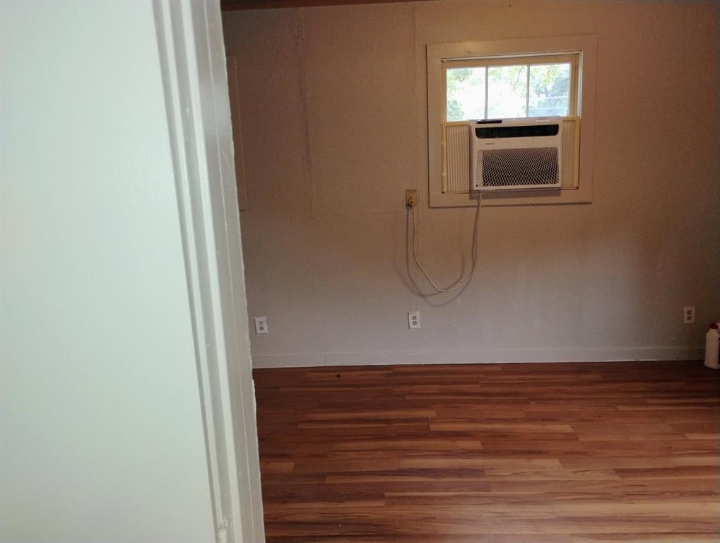 Interior room featuring wood-finish flooring, a white-framed single-pane window, and a wall-mounted air conditioning unit