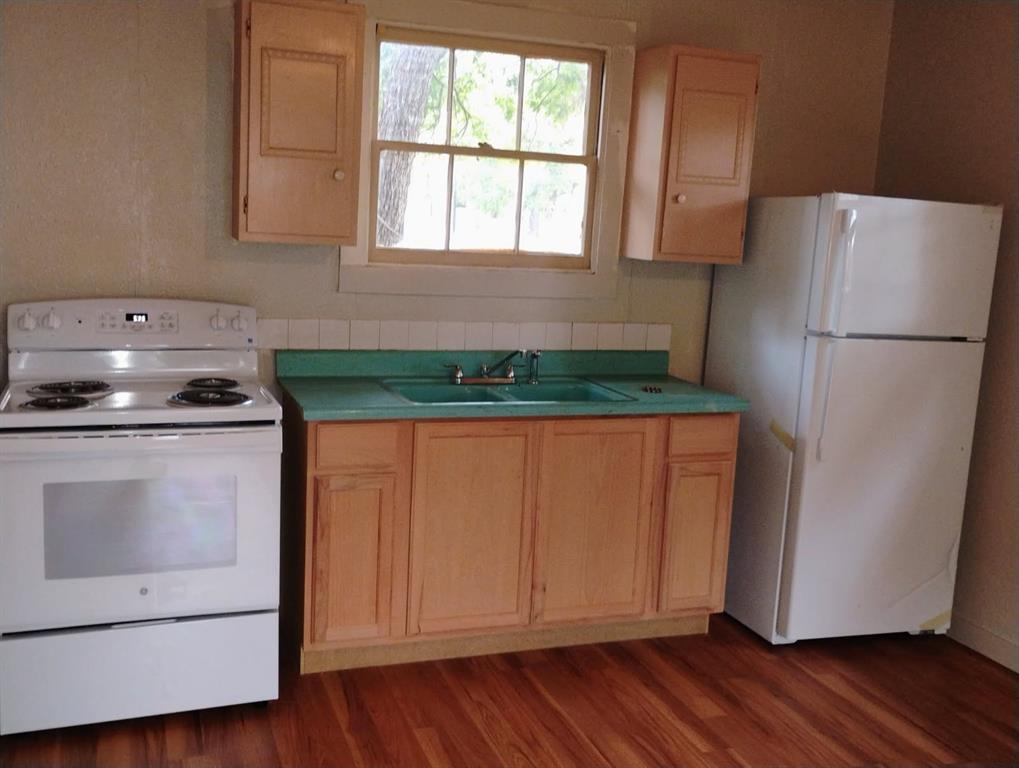 Kitchen featuring wood-finish flooring, wood cabinetry, a dual-basin sink, and white appliances