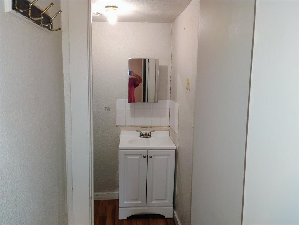 White vanity cabinet with an integrated basin, chrome-finish dual-handle faucet, mirrored medicine cabinet, and wood-finish flooring