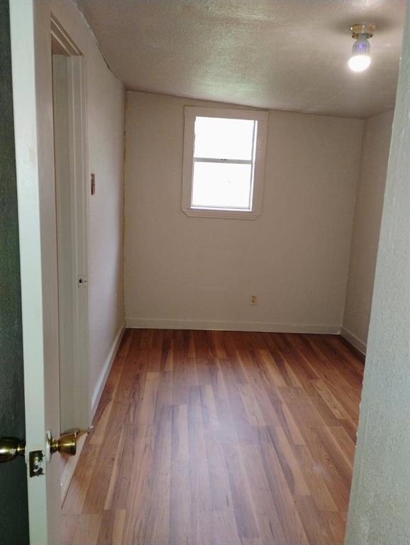 Room featuring wood-finish flooring, a single-pane window with white trim, and a ceiling-mounted light fixture