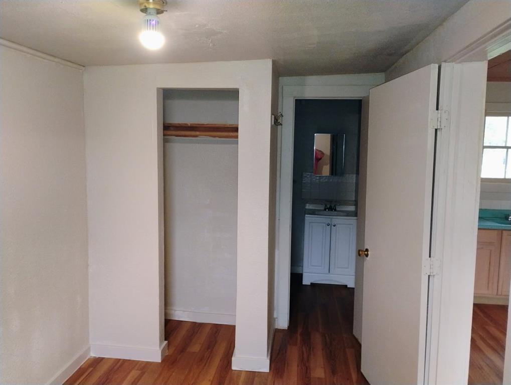 Room featuring wood-finish flooring, a built-in closet with a wooden shelf, and a ceiling-mounted light fixture