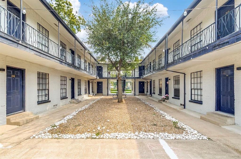 Exterior courtyard featuring white brick architecture, multi-level metal railings, grid-pattern windows, and a central gravel landscape design