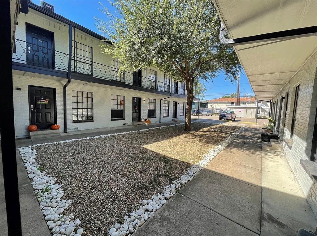 Multi-story exterior featuring painted brick, black metal balcony railings, a gravel courtyard with stone border, and concrete walkways