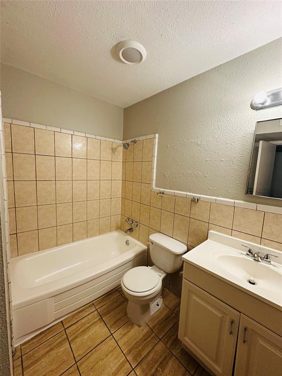 Bathroom featuring a tub with tile surround, wood-finish tile flooring, a white vanity with an integrated sink, a wall-mounted mirror, and overhead lighting