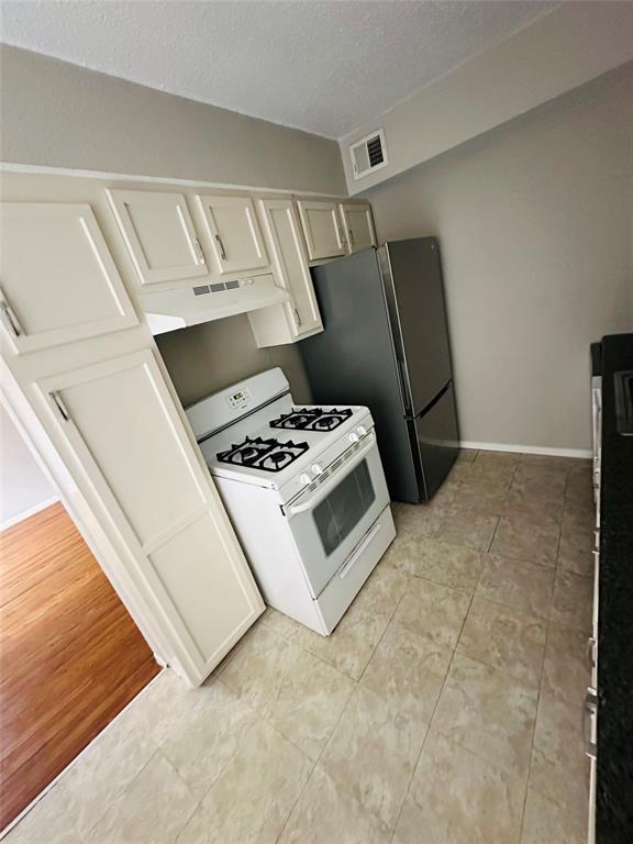 Kitchen featuring white cabinetry, a freestanding gas range, a stainless steel refrigerator, and stone-finish tile flooring