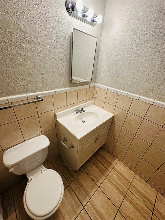 Vanity cabinet with an integrated sink and chrome faucet, mounted medicine cabinet, three-light fixture, and ceramic tile wainscoting