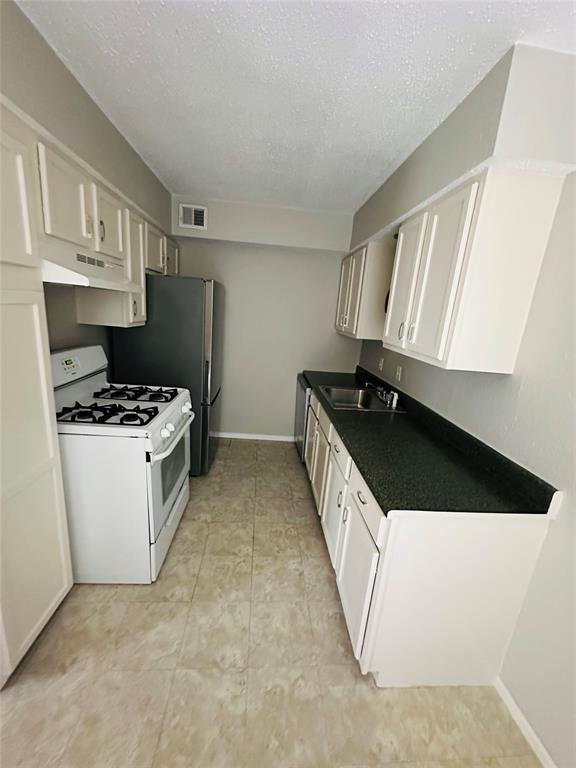 Galley kitchen featuring white cabinetry, dark countertops, a stainless steel sink, a four-burner gas range, and ceramic tile flooring