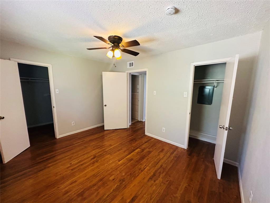 Room featuring wood-finish flooring, two closets with built-in shelving, and a ceiling-mounted light fixture with a fan